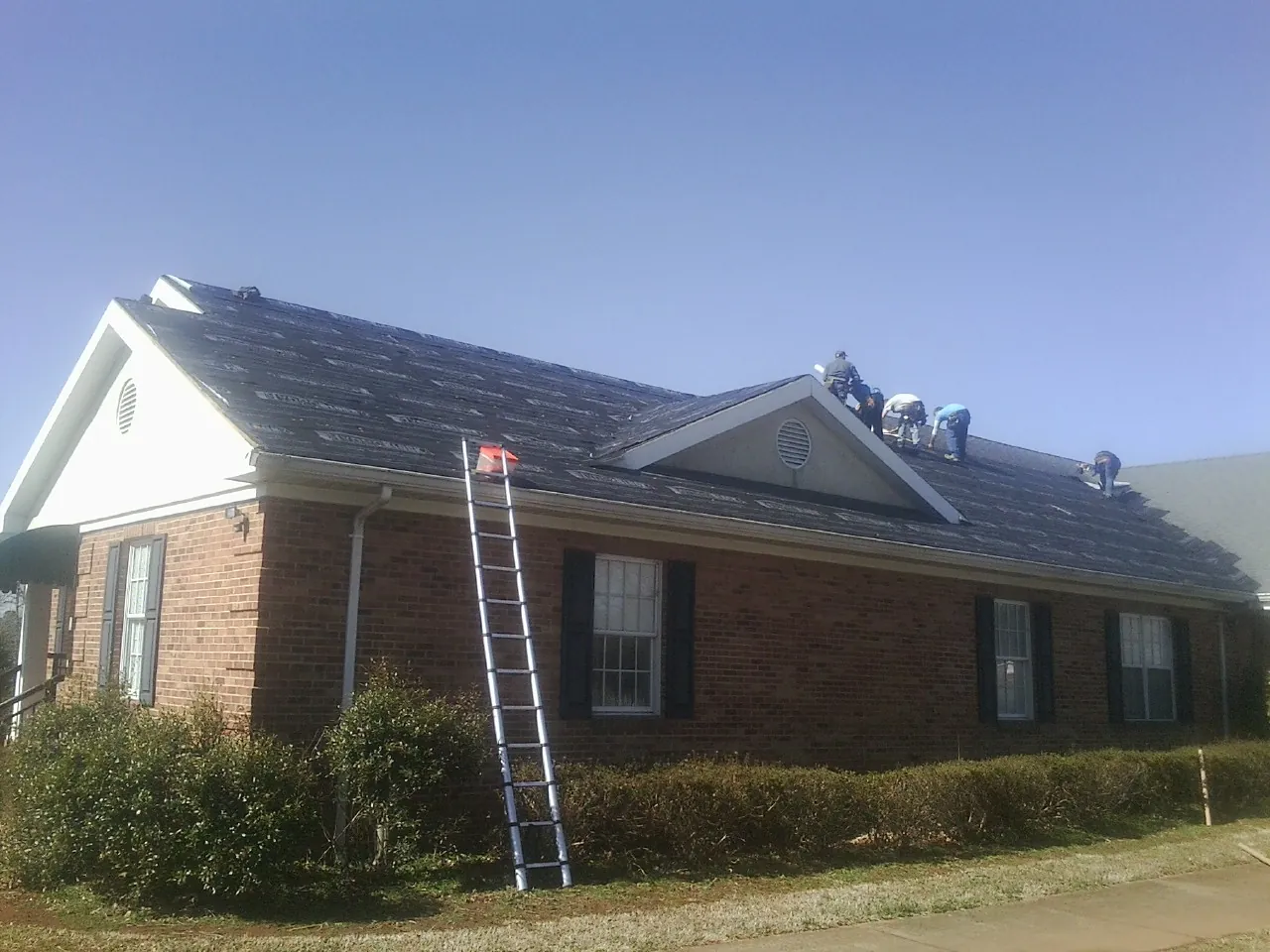 Crew tearing shingles off a brick ranch roof with a ladder set — Emergency Roof Repair work by our crew in Ocean Springs