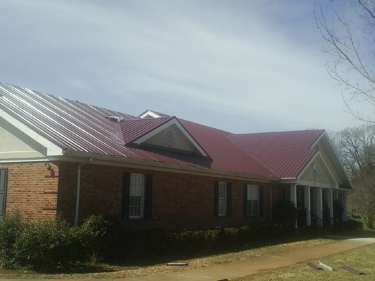 Red metal roof with gabled entries on a long brick building, from a Hail Damage Roof Repair job in Ocean Springs