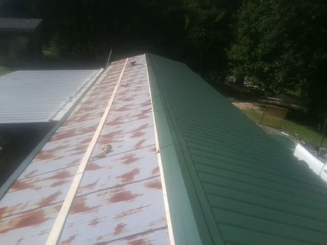 Old rusted panels beside newly installed green metal roofing — Wind Damage Roof Repair by Roofing Brothers in Ocean Springs
