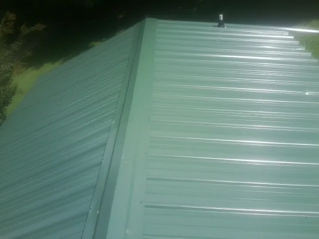 New green metal panels meeting at the ridge of a roof — Flat Roof Repair work by our crew in Ocean Springs