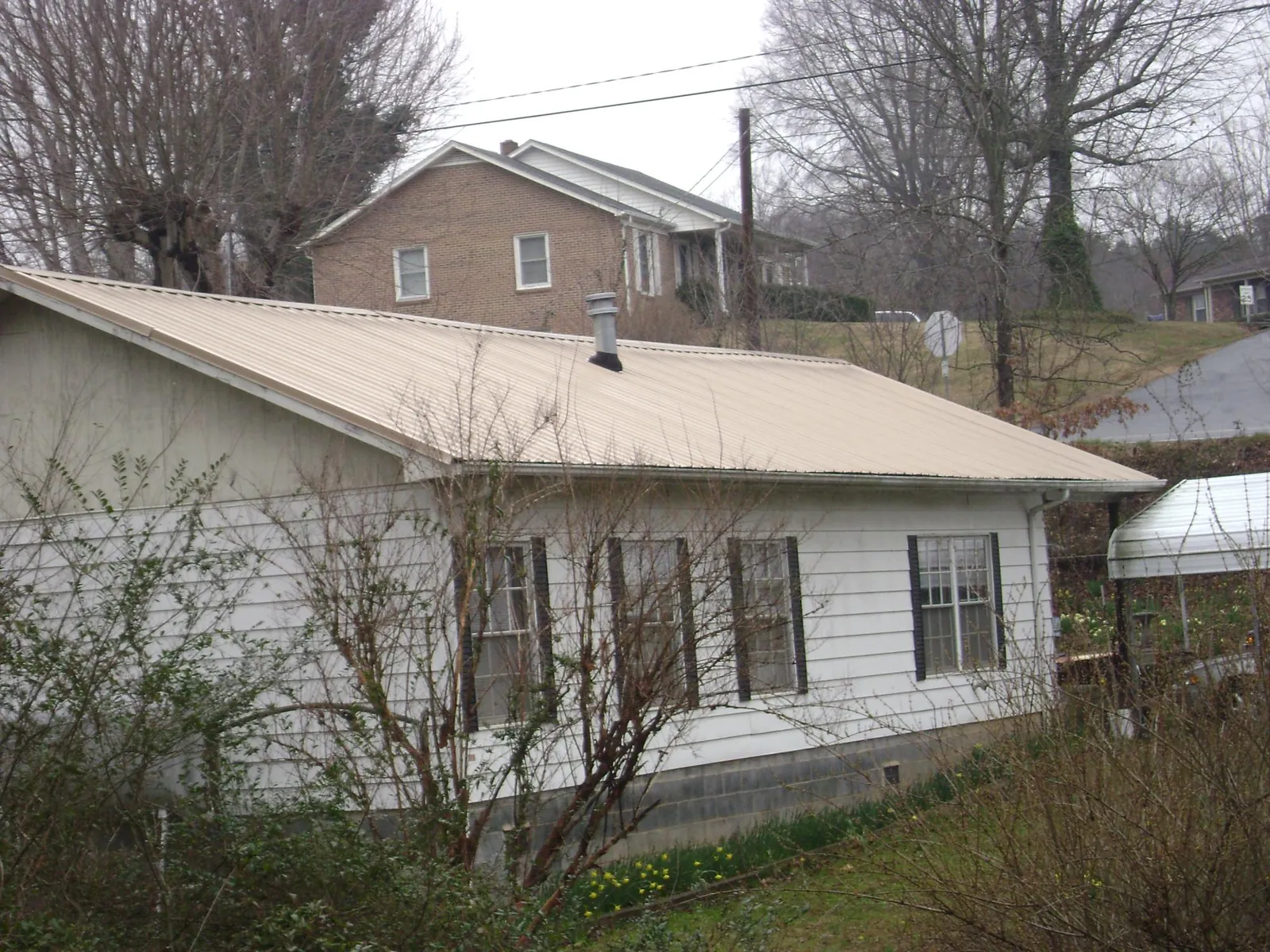 Tan metal roof on a white sided house set into a hillside — Commercial Roofing by Roofing Brothers in Ocean Springs